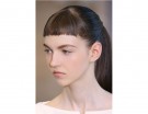 Capelli lunghi raccolti in una coda, con frangia corta e pari.