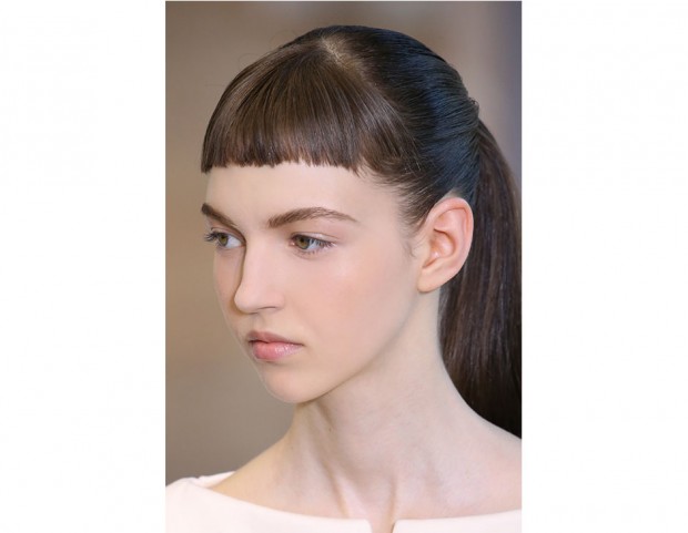 Capelli lunghi raccolti in una coda, con frangia corta e pari.