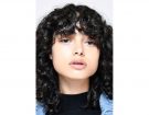 Long bob e frangia piena con i capelli ricci fitti.